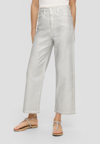 Hochgeschnittene, weit geschnittene Jeans aus hellgrauem Denim mit einer glatten Textur, ausgestattet mit Fronttaschen und Gürtelschlaufen. Dazu werden flache Sandalen getragen.