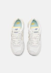 Vita mockasinsneakers med gula och grå accenter, med en vadderad tunga, snördesign och en vadderad inredning. Modell 574.