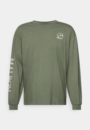 Tričko s dlhým rukávom z olivovozelenej bavlny. Na hrudi má malý biely grafický motív a na ľavom rukáve detailný biely dizajn.