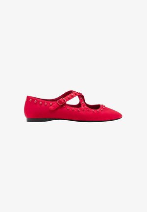 Chaussure plate rouge à bout pointu, bride de cheville avec boucle, et ornements à clous ronds le long des bords et de la bride, semelle noire, vue de côté.