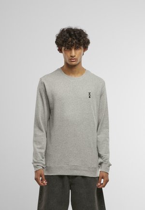 Pullover grigio con maniche lunghe, scollo rotondo e polsini a coste. Caratterizzato da un piccolo logo nero "K" sul lato sinistro del petto. Texture morbida.
