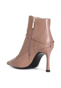 Bota corta de cuero marrón con punta afilada, diseño elegante, cremallera lateral y tacón de aguja, con una superficie texturizada y detalles mínimos.