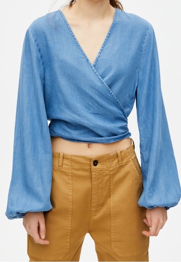 Haut cache-cœur en denim bleu clair à manches longues bouffantes et décolleté en V profond, associé à un pantalon taille haute couleur sable.