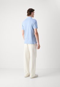 Polo shirt azzurro chiaro con colletto bianco a contrasto, abbinato a pantaloni bianchi larghi e scarpe chiare, visto da dietro.