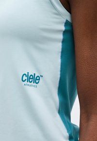 Εγγύς λήψη ενός αμάνικου αθλητικού τοπ σε ανοιχτό μπλε χρώμα με το λογότυπο "ciele athletics" και τυρκουάζ πλαϊνή πινελιά στον βραχίονα και τον ώμο ενός ατόμου.
