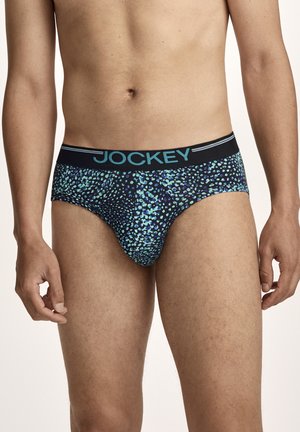 Männlicher Torso, der schwarze Slips mit blau-grünem Punktmuster und einem schwarzen Bund trägt, auf dem „Jockey“ in blauen Buchstaben steht.