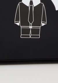 Grafisk design av en figur i kostym och slips, konturerad i vitt, mot en svart bakgrund, med blockiga former och minimala detaljer.