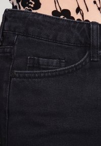 Jean en denim foncé au design classique, avec une poche avant, des coutures robustes et une texture lisse. Le tissu semble durable et flexible.