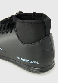 Chaussure de football synthétique noire avec une tige haute, surface texturée, lacets noirs, accents bleus et logo. Semelle en caoutchouc, conçue pour le jeu en intérieur.