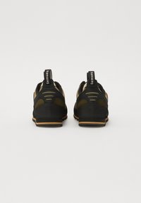 Schwarze und olivgrüne Wanderschuhe mit einem strukturierten Obermaterial, verstärkten Fersen und kontrastierenden Gummisohlen. Mit Zugschlaufen an der Rückseite.