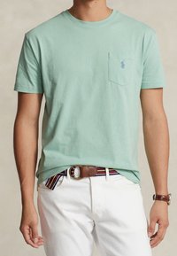 Mintgrön bomull t-shirt med korta ärmar, med en bröstficka och en liten logotyp. T-shirtens styling kompletteras med vita byxor och ett flerfärgat randigt bälte.