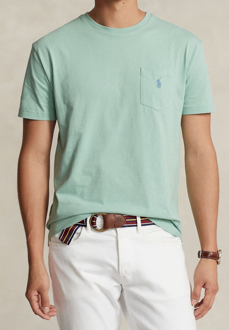 Mintgrön bomull t-shirt med korta ärmar, med en bröstficka och en liten logotyp. T-shirtens styling kompletteras med vita byxor och ett flerfärgat randigt bälte.