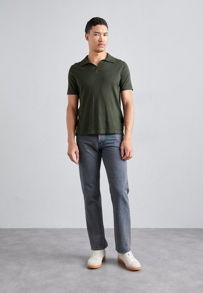 Polo de manga corta color verde oliva con cuello plano, combinado con jeans rectos de color gris claro y zapatillas de tonalidad clara.
