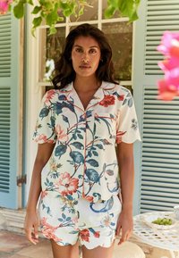Pajama set w usłanym wzorem kwiatowym, wykonany z lekkiego materiału. Top z krótkim rękawem ma kieszonkę i czerwone wykończenie, zestawiony z szortami z falbaniastym wykończeniem.