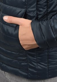 Granatowa puchówka z poziomym przeszyciem, z boczną kieszenią i dopasowanym mankietem. Gładka, błyszcząca tekstura.