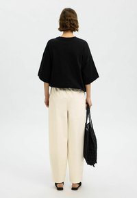 T-shirt noir oversize à manches courtes, associé à un pantalon large crème et un sac fourre-tout tressé noir. Tissu lisse avec une coupe décontractée.