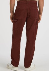Bordeaux corduroy broek met een rechte pijp, voorzien van twee grote zijzakken en achterzakken, gecombineerd met witte sneakers.