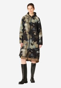 Abrigo acolchado con capucha que presenta un patrón floral multicolor en tonos de verde, negro y crema. La longitud llega hasta medio pantorrilla.