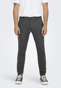 Grå slim-fit byxor gjorda av mjukt tyg, med knappstängning, bälteshällor och en slät yta, i kombination med svarta sneakers.