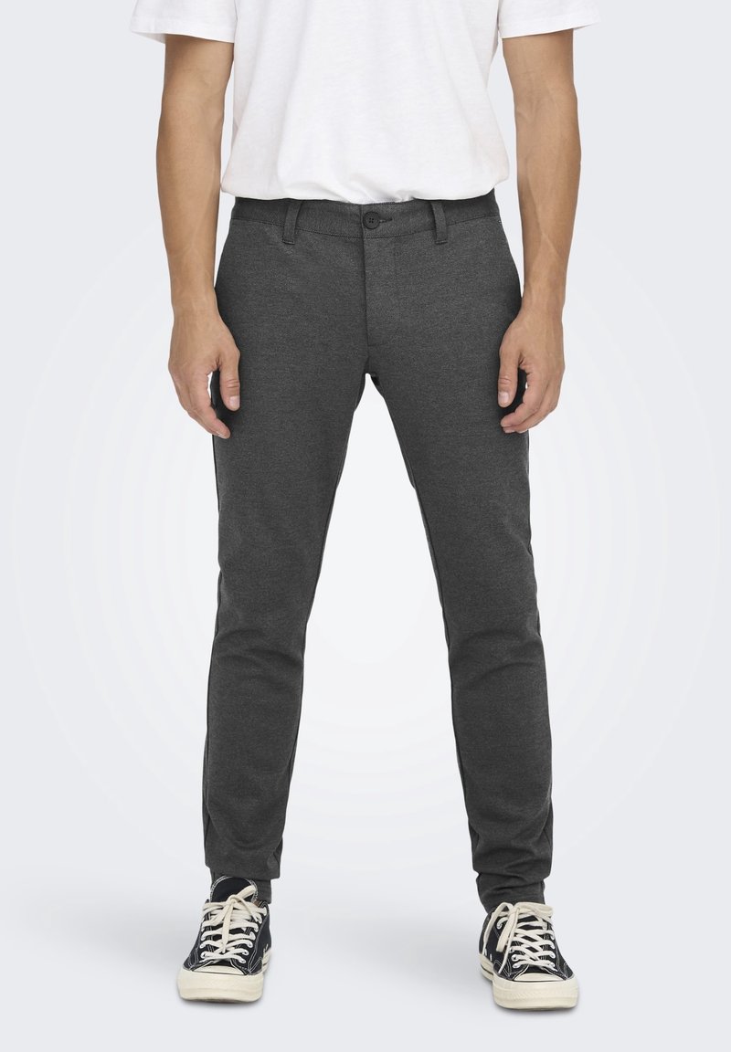 Grå slim-fit byxor gjorda av mjukt tyg, med knappstängning, bälteshällor och en slät yta, i kombination med svarta sneakers.