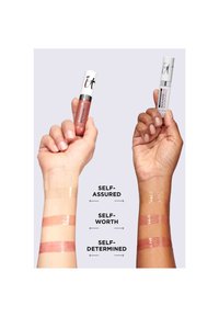 Deux mains tenant des tubes de gloss à lèvres avec trois échantillons de gloss assortis étiquetés Confiant, Estime de soi et Déterminé, appliqués sur différentes nuances de peau.
