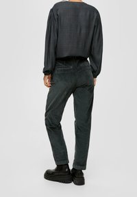 Blouse à carreaux foncés avec des manches bouffantes et un ourlet court, associée à un pantalon en velours côtelé vert foncé avec une texture côtelée verticale. Bottes épaisses noires.