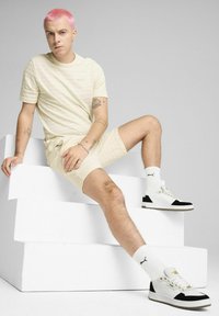 Lys beige stribet t-shirt og shorts lavet af åndbart stof, parret med hvide og sorte sneakers, der hviler på hvide trin.