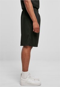 Shorts de sport noirs avec une taille élastique, poches latérales et texture lisse, associés à des baskets blanches et des chaussettes de cheville.