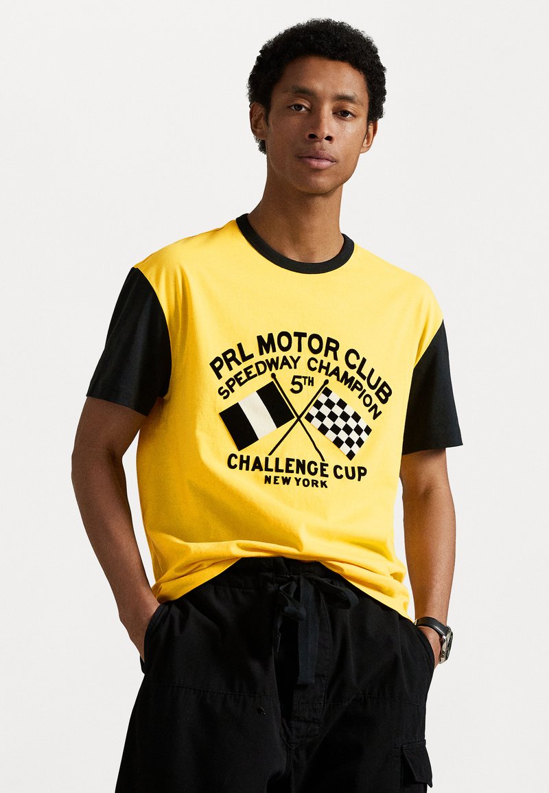 Gul og svart kortermet t-skjorte med "PRL MOTOR CLUB" trykk, rutete flagg og teksten "CHALLENGE CUP NEW YORK".