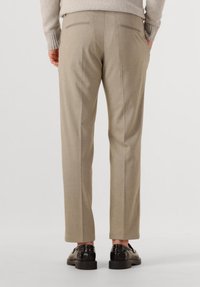 Beige tailored trousers featuring a straight fit, subtle texture, and two back pockets; paired with shiny black shoes.