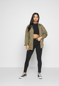 Maslinasto zelena oversized jakna preko crnog crop topa, uparena s crnim uskim trapericama i crnim tenisicama. Glatke teksture, ležeran dizajn.