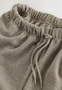 Szare bawełniane spodnie dresowe z elastycznym paskiem w talii z marszczonym wykończeniem oraz sznurkiem do regulacji. Gładki, miękki materiał.