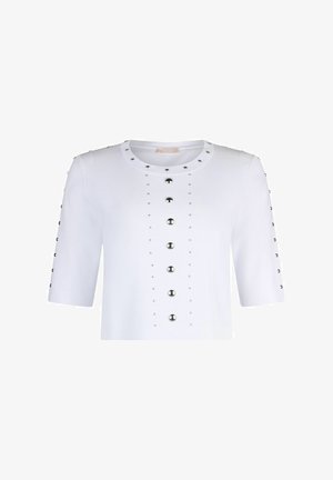 Haut blanc à manches courtes avec un col rond, orné de clous métalliques formant une ligne verticale au centre et sur les manches.