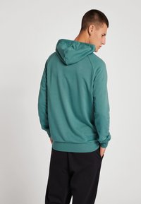 Türenfarbene Kapuzenjacke mit Kängurutasche und gerippten Bündchen. Verfügt über eine gefütterte Kapuze und einen lockeren Schnitt. Der Stoff wirkt weich und glatt.