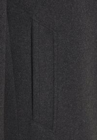 Abrigo de lana gris con una superficie texturizada, que presenta un bolsillo rectangular en la parte frontal y un diseño entallado, que enfatiza sus líneas limpias.