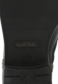 Sort skosål med "Gusti Leder" logo og størrelse 38 præget i midten af sålen.