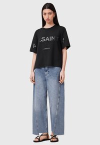 Sort bomulds t-shirt med oversized pasform og trykt "ALSAINTS LONDON" logo, parret med lysblå brede jeans og sorte sandaler.