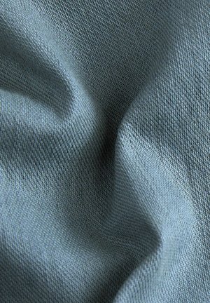 Tekstureeritud kangas pehme sinise tooni ja kootud mustriga, millel on sile viimistlus ja peen sära, näidates õrnu voldikesi ja kortsud.