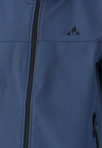 Blå jacka med dragkedja fram, textil med struktur och svarta detaljer. Framträdande logotyp på övre vänstra sidan. Fickor med dragkedja på sidan.