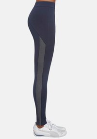 Granatowe legginsy z teksturowanym, ukośnym bocznym panelem z małymi perforacjami; wysoki pas; w połączeniu z białymi butami sportowymi.