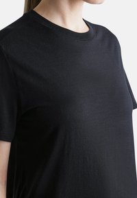 Black cotton T-shirt with short sleeves, crew neck design, slightly textured surface, and a loose fit, shown from the side.