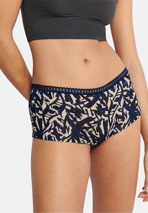 Vrouw draagt beige en marineblauwe gebloemde slip met kanten rand en een zwarte cropped top, torso en bovenbenen zichtbaar.