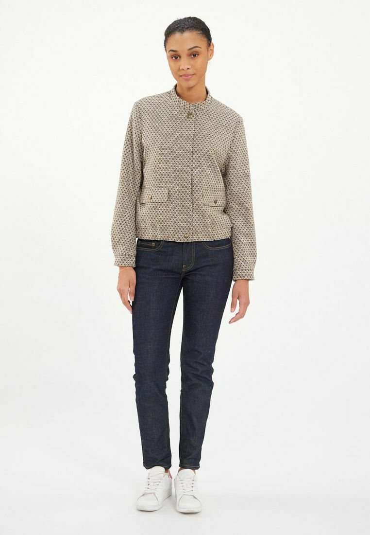 Veste bomber à motifs beige avec un col arrondi, deux poches avant et fermeture à boutons, assortie à un jean bleu foncé et des baskets blanches.