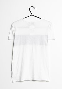 Biała bawełniana koszulka wisząca na czarnym haczyku, z prostym wzorem i delikatną teksturą gradientu w centrum. Brak grafik czy wzorów.