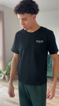 Čierne bavlnené tričko s krátkymi rukávmi a okrúhlym výstrihom, s bielym nápisom na ľavej hornej časti; nosené so zelenými teplákmi.