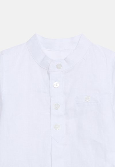 Λευκό λινό πουκάμισο με γιακά μανταρίνι, εμπρόσθια σειρά κουμπιών με τέσσερα κουμπιά και μικρή τσέπη στο στήθος με κουμπί.