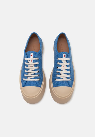 Blue denim sneakers with beige rubber sole, white laces, and red accents on the tongue. Features a smooth texture and classic low-top design.