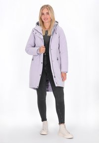 Svijetlopurple zaštitna jakna s kapuljačom, zatvaranjem na munju i komande, bočnim džepovima, nosi se preko crnih traperica i bež visokih tenisica.