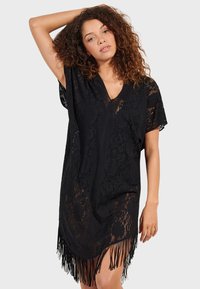 Vestido de encaje negro con mangas cortas, escote en V y detalles de flecos en el dobladillo. Presenta un intrincado patrón floral en toda la prenda.