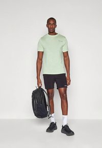 Gaiši zaļa īsroku krekls ar smalku tekstūru, kopā ar melniem šortiem. Melna mugursoma ar pelēkiem akcentiem, melni sporta apavi un baltas zeķes.